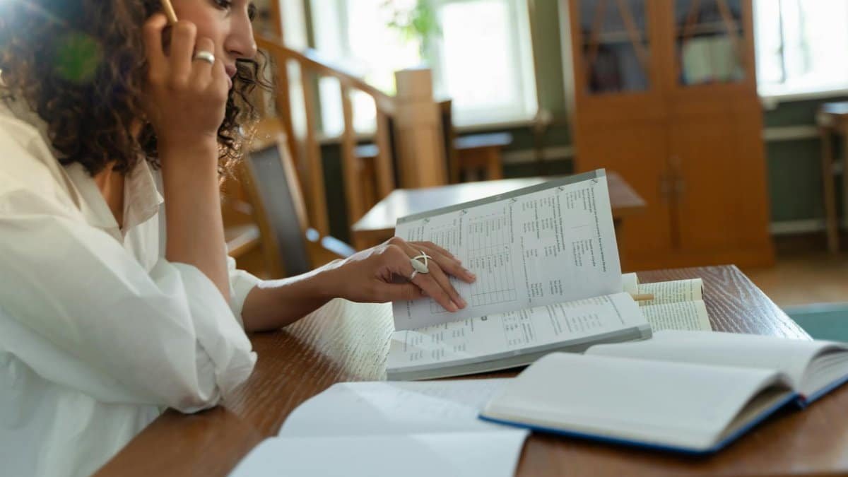 Focused woman studying with books in a cozy library, enhancing learning and knowledge.