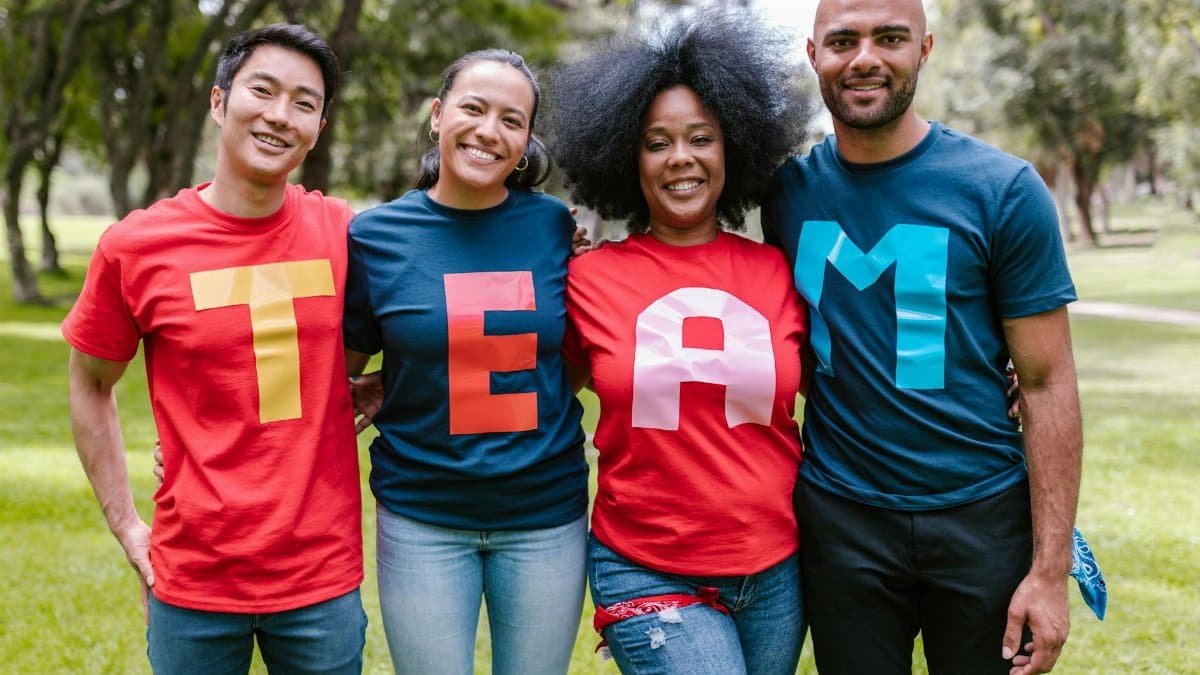 A diverse group of adults bonding and smiling in a park wearing TEAM shirts.