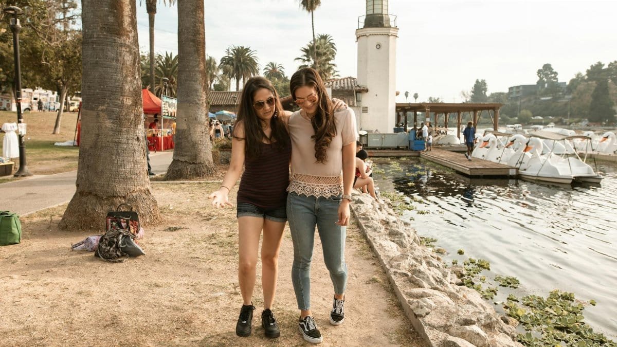 Two women enjoy a sunny walk by the lakeside, showcasing friendship and leisure.