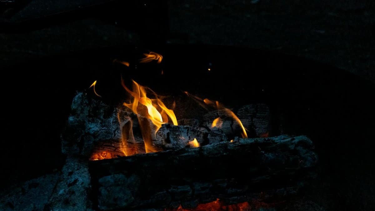 A close-up view of a bonfire with glowing embers and bright flames, creating warmth on a dark night.