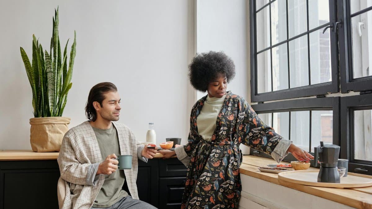 A couple enjoys morning coffee together by a large window, capturing a peaceful everyday life moment.