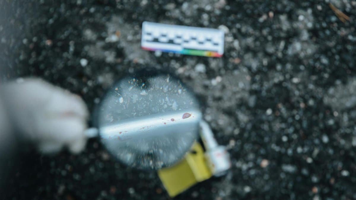Close-up of evidence analysis at a crime scene with a magnifying glass.