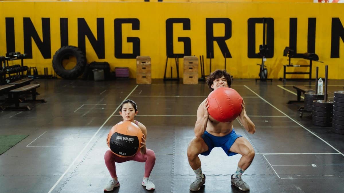 Asian couple performing squats with medicine balls indoors. Perfect for fitness-related concepts.