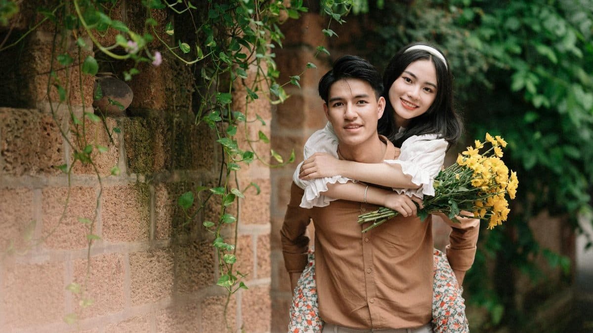 A happy young couple with flowers, enjoying a romantic moment outdoors by a brick wall.