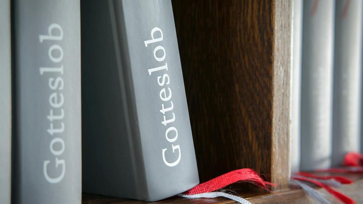 Close-up of Gotteslob hymn books with red bookmarks on wooden shelf.