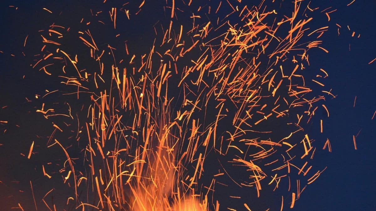 Vibrant orange sparks fly from a fire against a dark blue night sky, creating a dramatic visual.