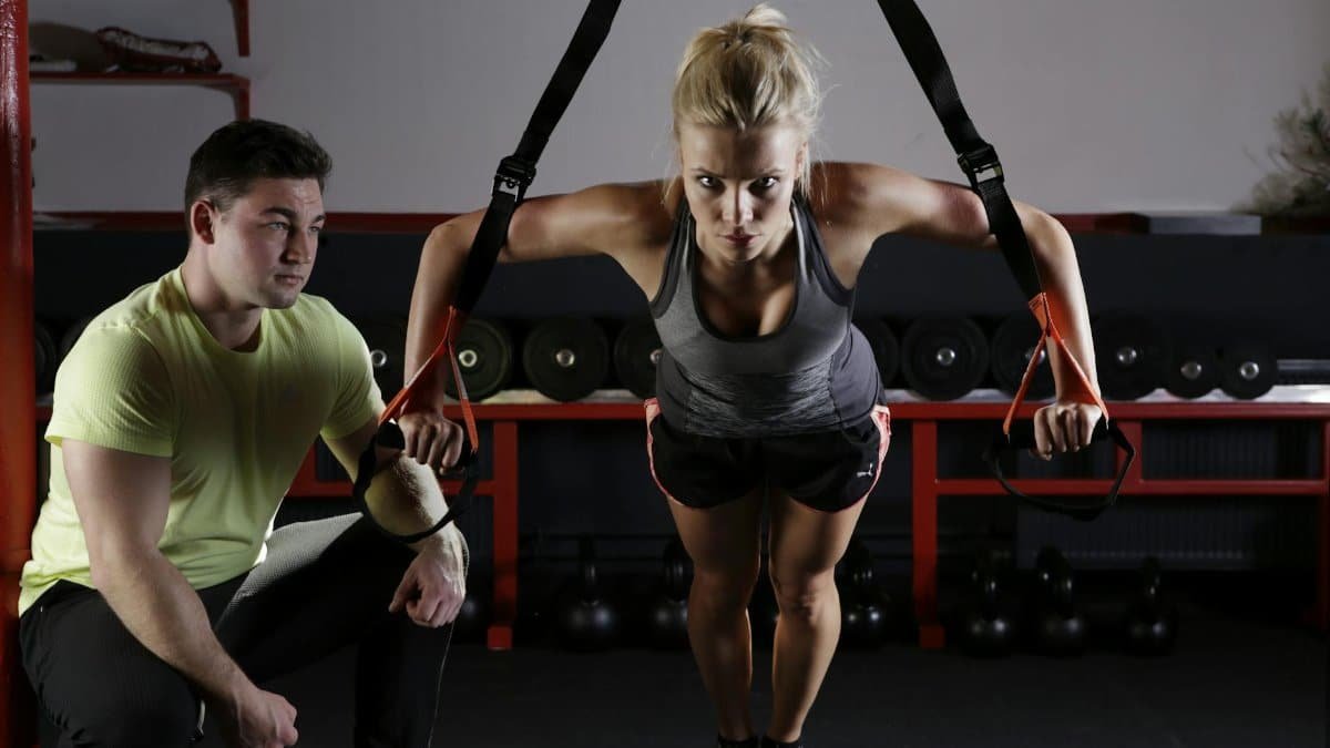 A woman performing strength training with a trainer in a gym setting, showcasing fitness and dedication.