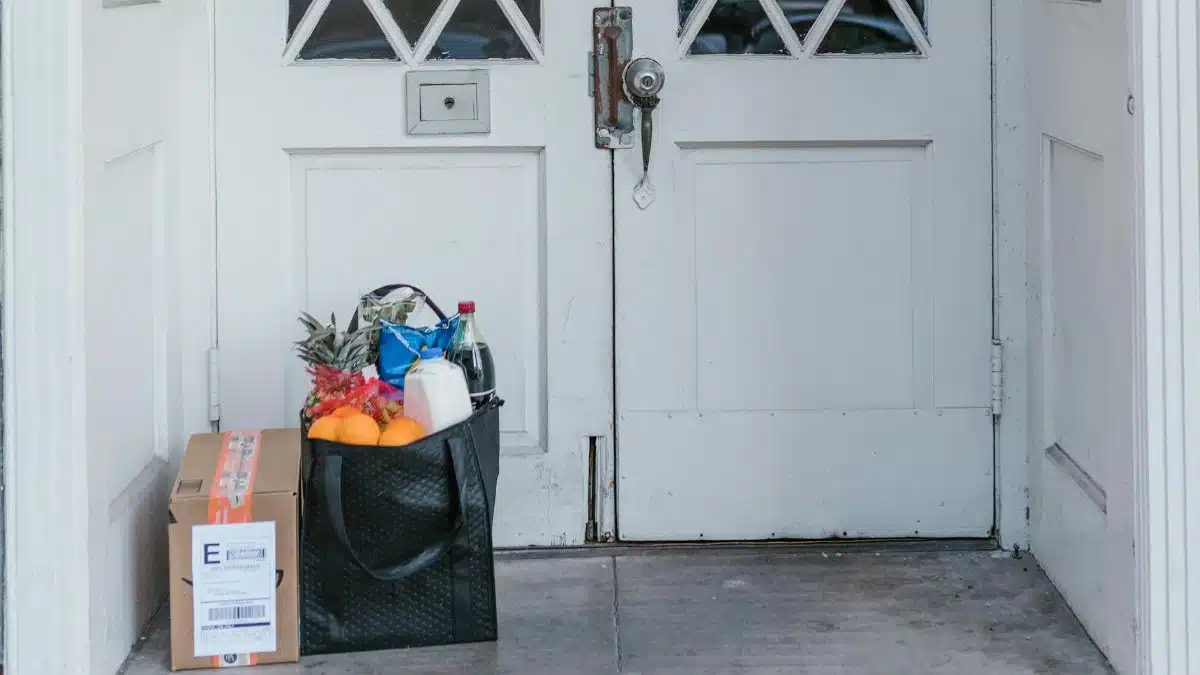 Front doorstep with grocery bag and parcel, representing contactless home delivery services.