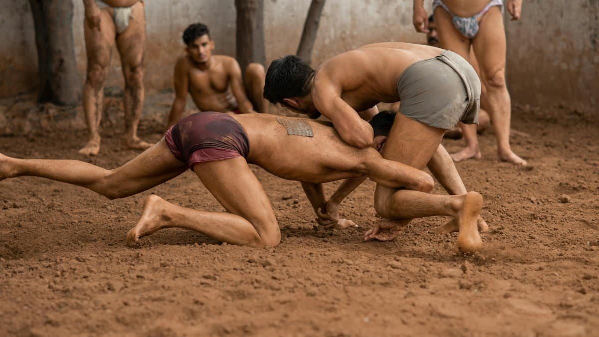 Two men engage in traditional Indian wrestling in a mud arena, showcasing skill and culture.