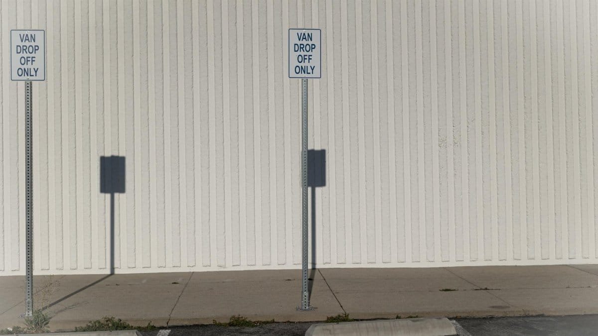 Van drop off only zone in an urban parking area with shadows and signs.