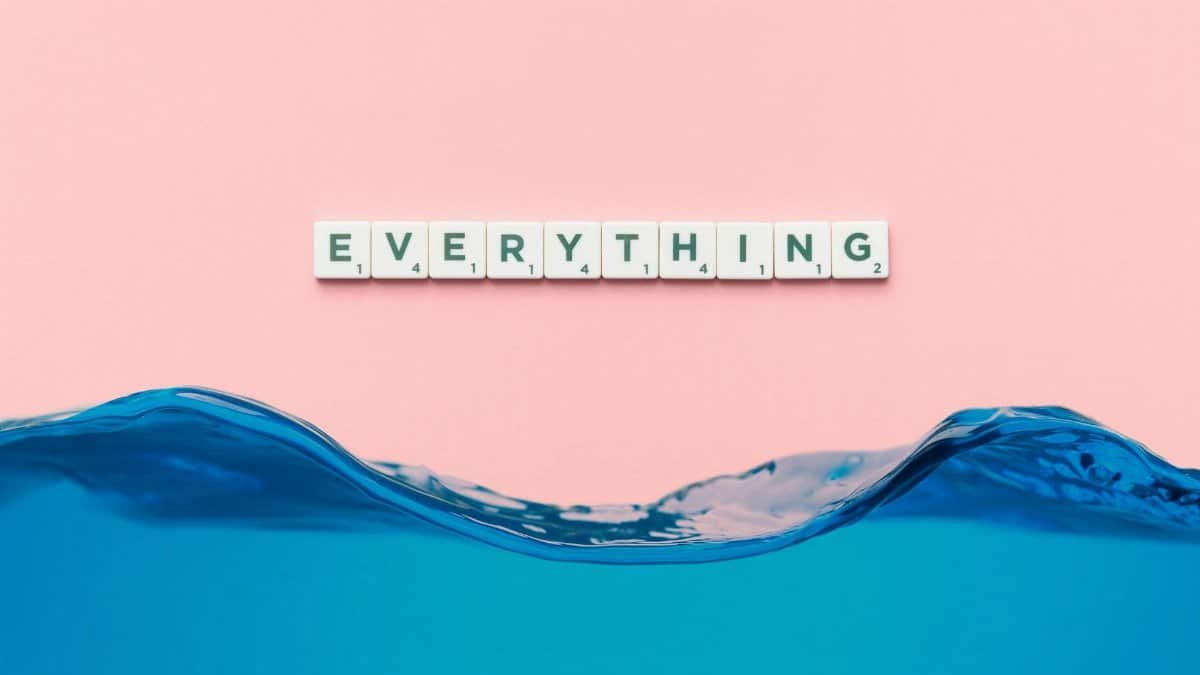 Scrabble tiles spelling 'everything' float above a blue wave on a pink background.