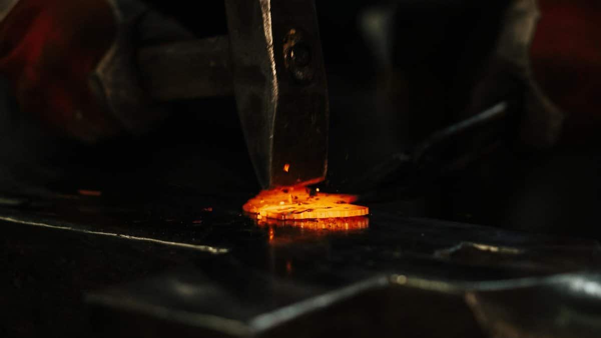 High angle of crop anonymous male blacksmith using hammer while forging metal detail in workshop