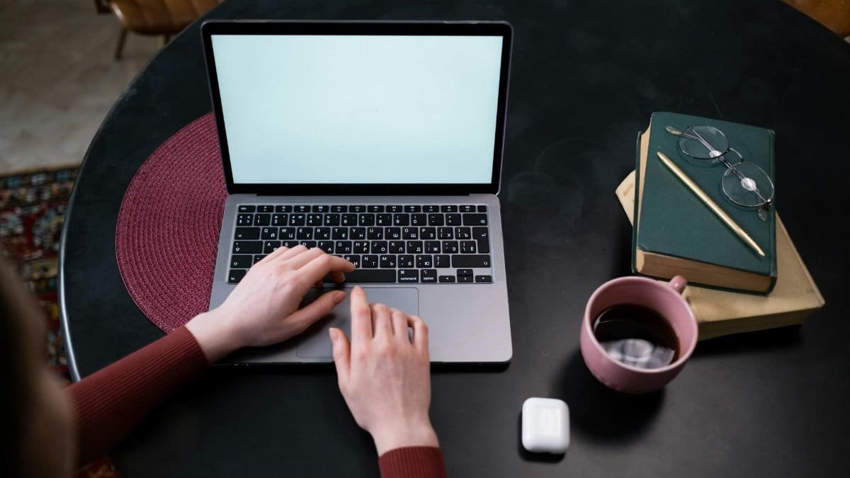 Hands typing on a laptop at a stylish indoor workspace with coffee and books.