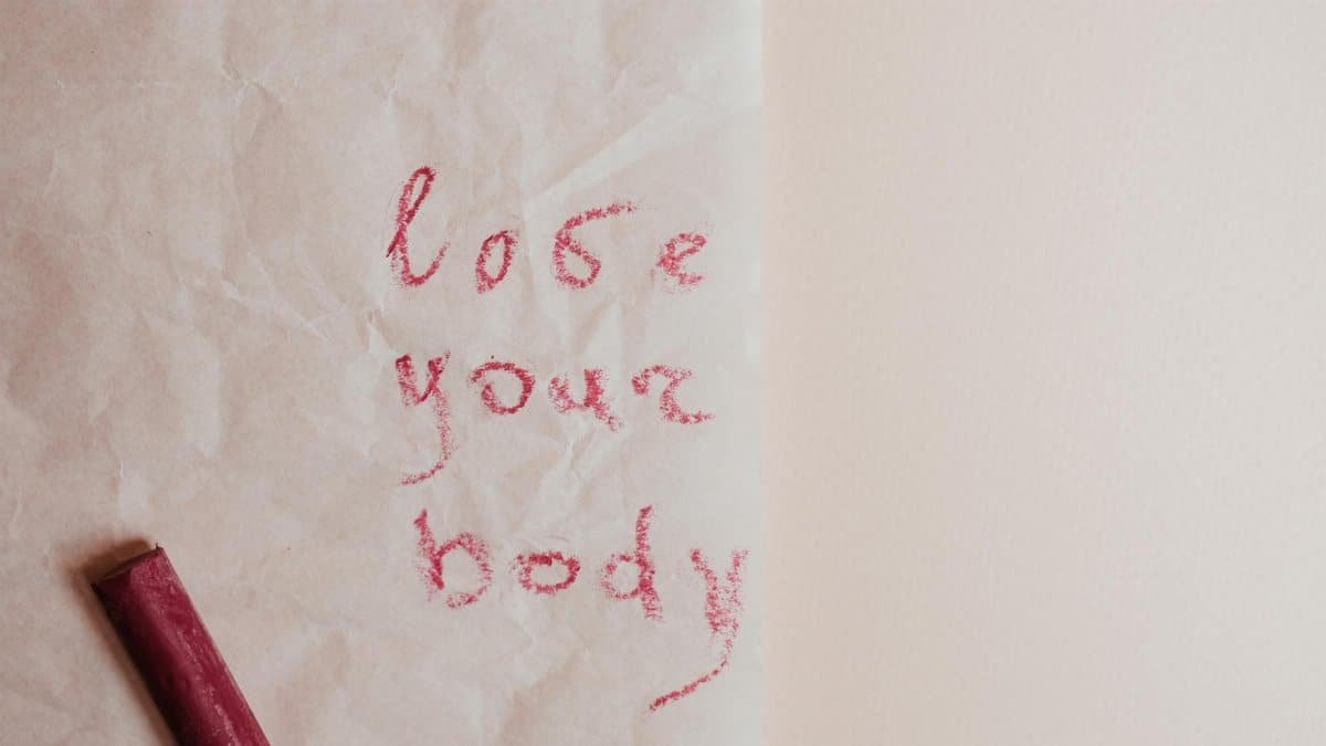An inspiring 'love your body' message written on textured paper with red pastel crayon.
