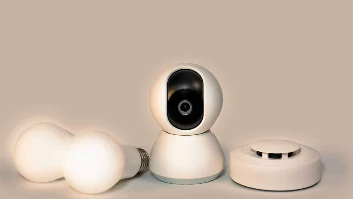 A collection of modern smart home gadgets including a CCTV camera, LED bulbs, and a smoke detector.