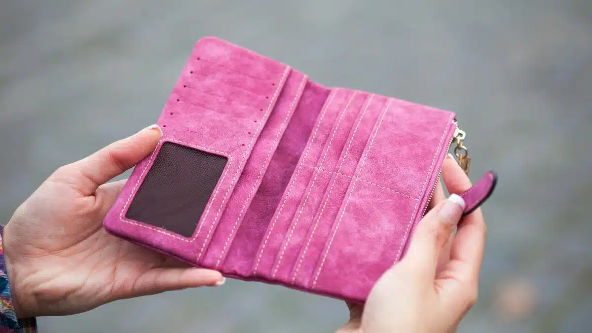 A woman holds an open, empty pink wallet outdoors, emphasizing financial themes.