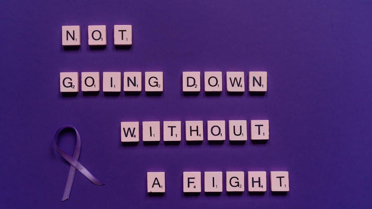 Scrabble tiles with an inspiring quote and a purple ribbon on a purple background.