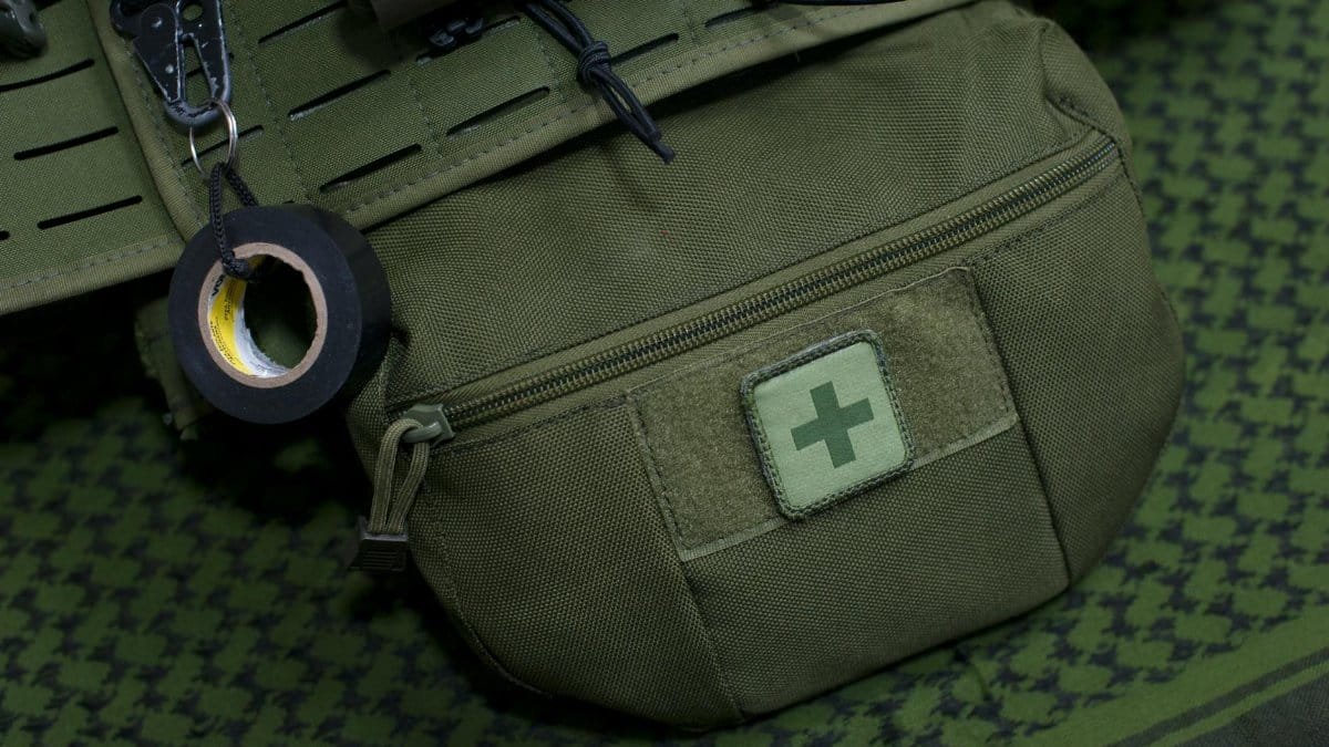 Close-up of a green first aid kit pouch attached to military gear, highlighting preparedness.