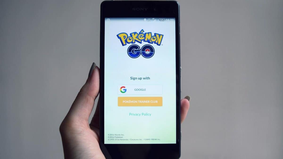 Smartphone displaying Pokémon Go app sign-in screen, held in hand.