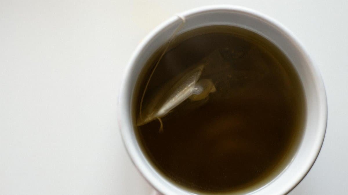 Top view of a white cup filled with fresh brewed green tea on a white background.