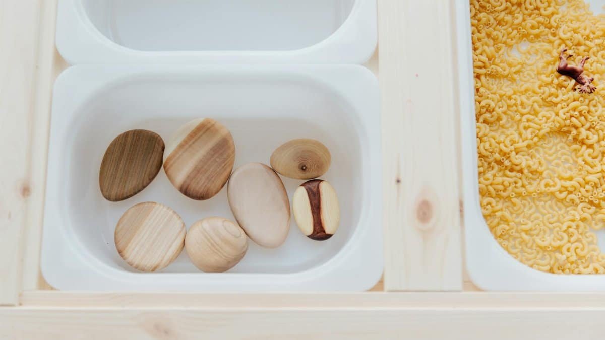 Top view of a creative sensory play setup with wooden objects and pasta for educational purposes.