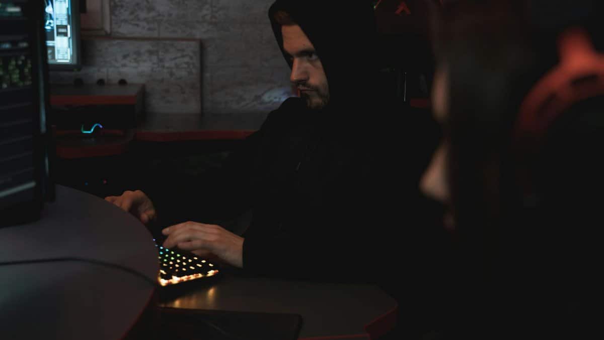 A man in a black hoodie works on a computer, focused on cyber security.