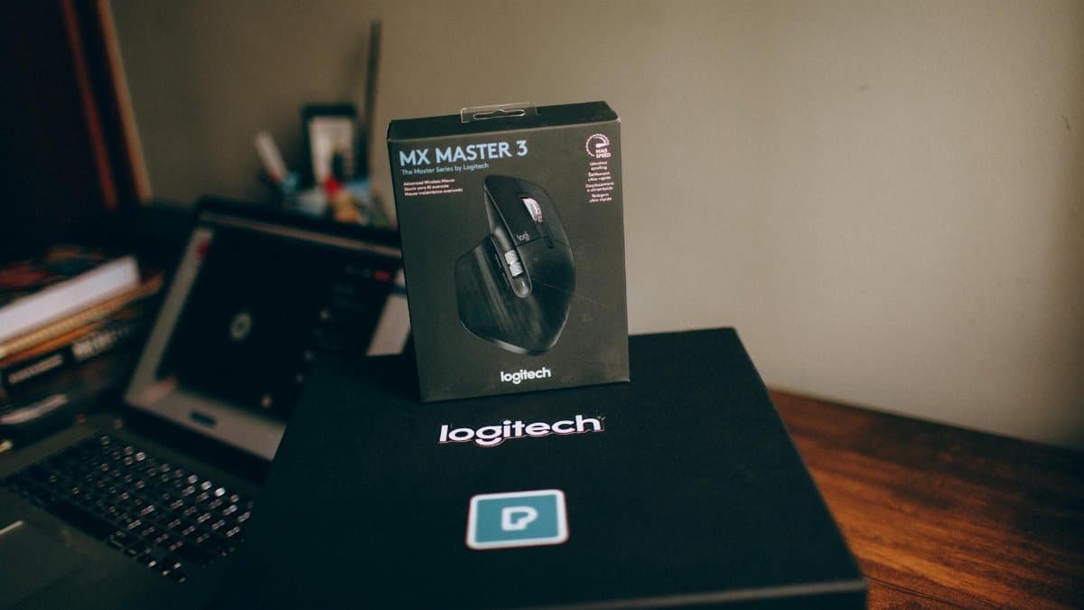 Image of Logitech MX Master 3 wireless mouse box on a desk with a blurred laptop in background.