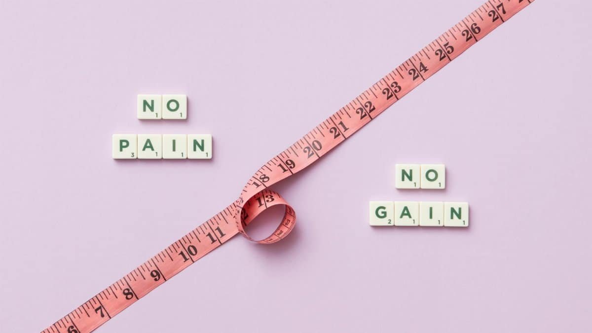 Pink tape measure with 'No Pain No Gain' spelled in Scrabble tiles on pink background.