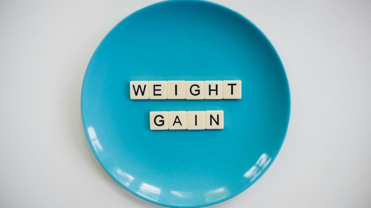 Scrabble tiles spelling 'weight gain' on a blue plate, symbolizing health and diet.