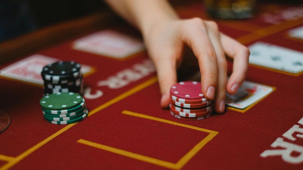 Hand handling poker chips on a casino table with cards, highlighting gambling activity.