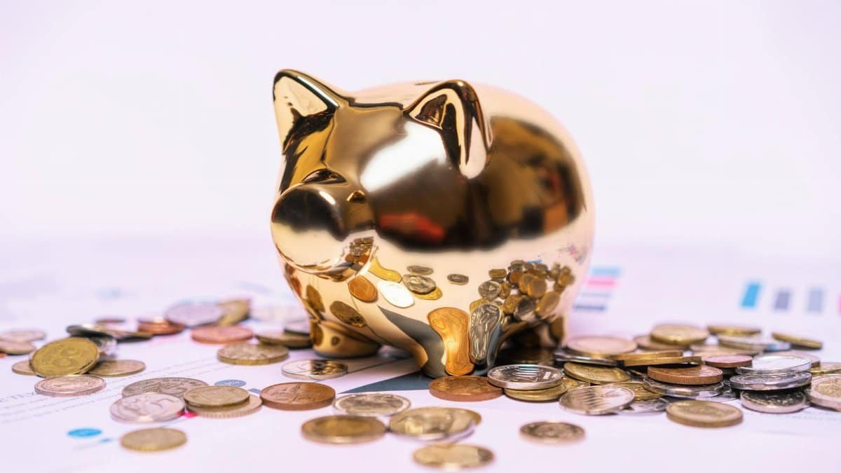 Shiny golden piggy bank on financial documents with scattered coins symbolizes savings.