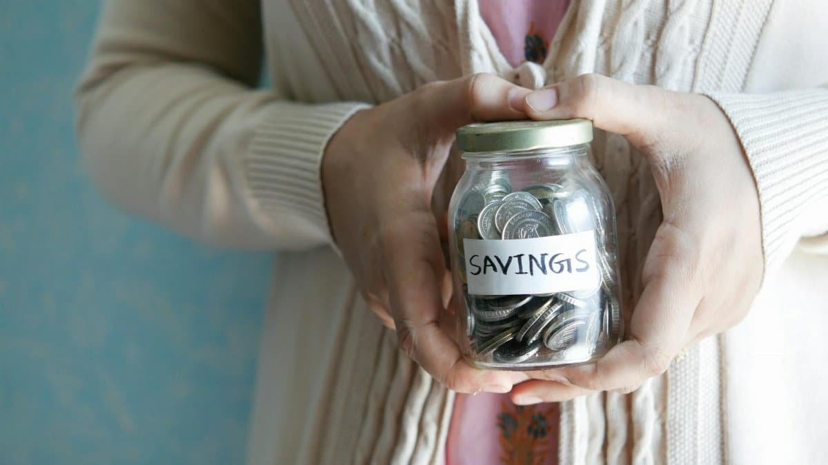Woman holding a jar labeled 'savings' filled with coins, representing financial savings.