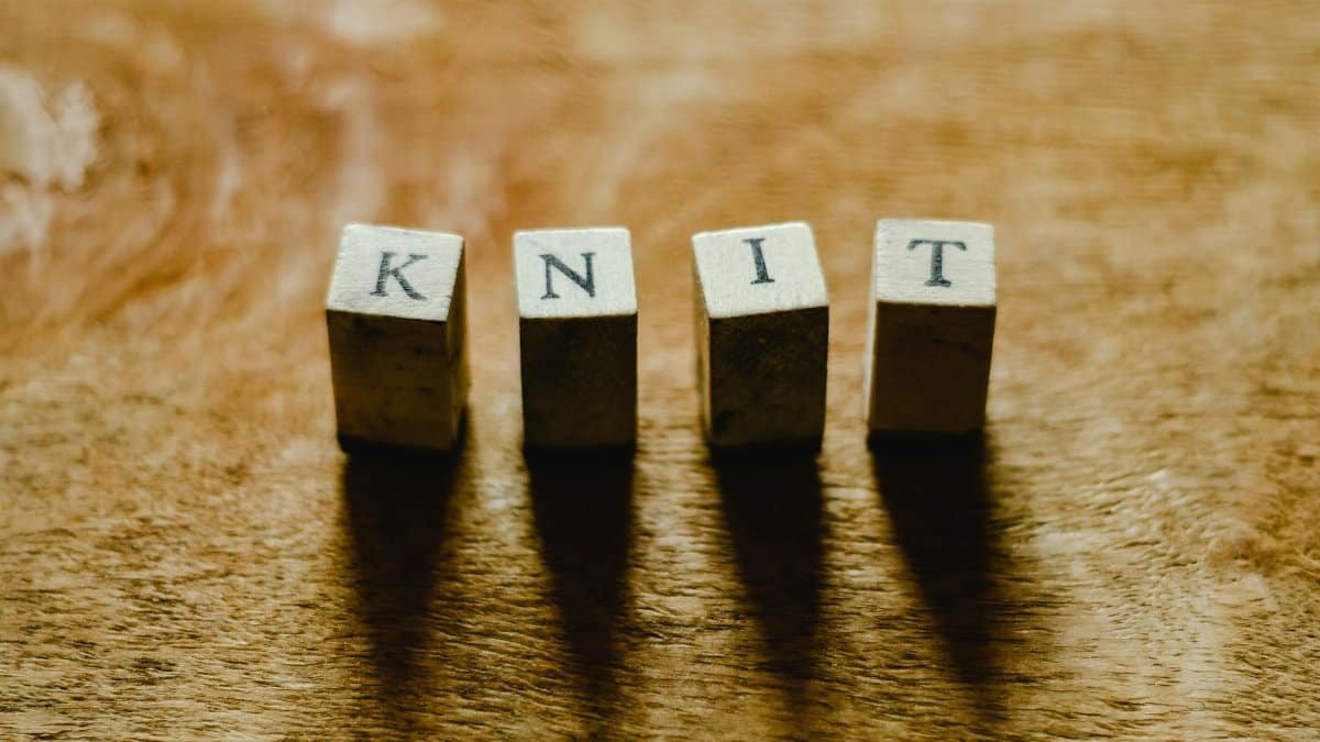 Close-up of wooden blocks spelling 'KNIT' on a textured wooden surface.