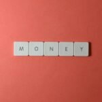 Minimalist layout showing word 'money' with letter tiles on a coral background.