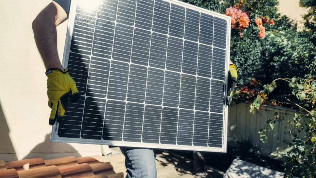 Technician carrying solar panel on rooftop. Clean energy installation outdoors.