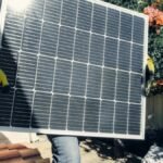 Technician carrying solar panel on rooftop. Clean energy installation outdoors.