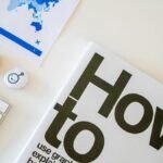 Stylish desk setup with a how-to book, keyboard, and world map on paper.