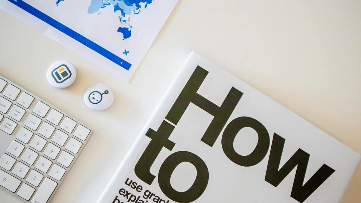 Stylish desk setup with a how-to book, keyboard, and world map on paper.
