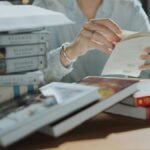 A young adult reading a book amidst a stack of books in a library, focusing on self-education and study.