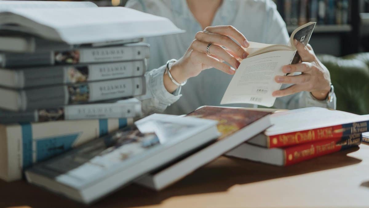 A young adult reading a book amidst a stack of books in a library, focusing on self-education and study.