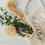 Eco-friendly cleaning brushes and eucalyptus branch in a net bag on a marble surface.