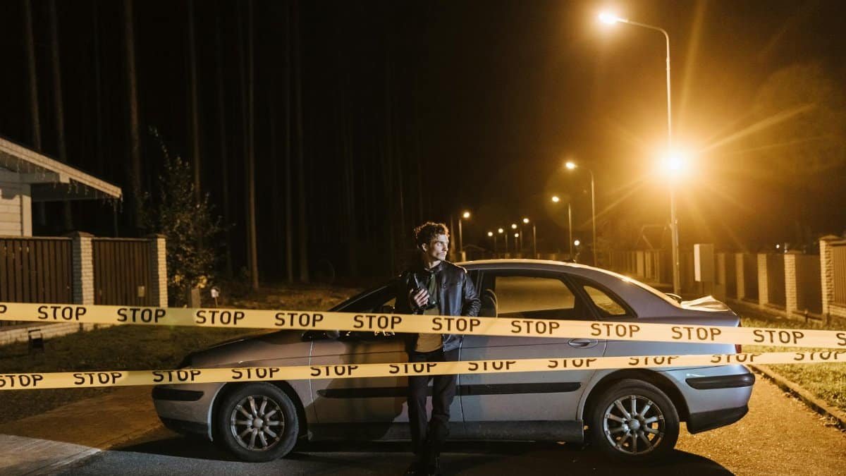 Man stands behind a car and stop tape at night, creating a mysterious scene.