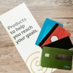Assorted credit cards on a wooden table next to a leaflet with motivational text about financial goals.