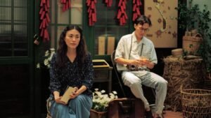 Two people in a vintage Asian room, surrounded by cultural decor, including a map and red decorations.