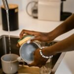 Close-up of woman washing dishes at kitchen sink, highlighting hands with bracelet.