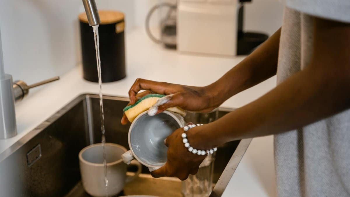 Close-up of woman washing dishes at kitchen sink, highlighting hands with bracelet.