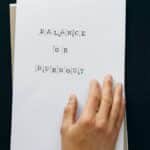 Hand holding paper with 'Balance or Burnout' text, promoting mental wellness.