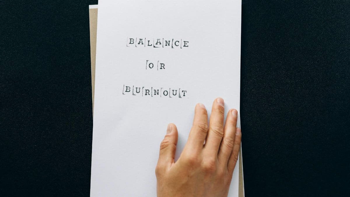 Hand holding paper with 'Balance or Burnout' text, promoting mental wellness.