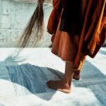 A Buddhist monk sweeping the marble courtyard in Bodhgaya, India. Captured in sunlight, highlighting spiritual simplicity.