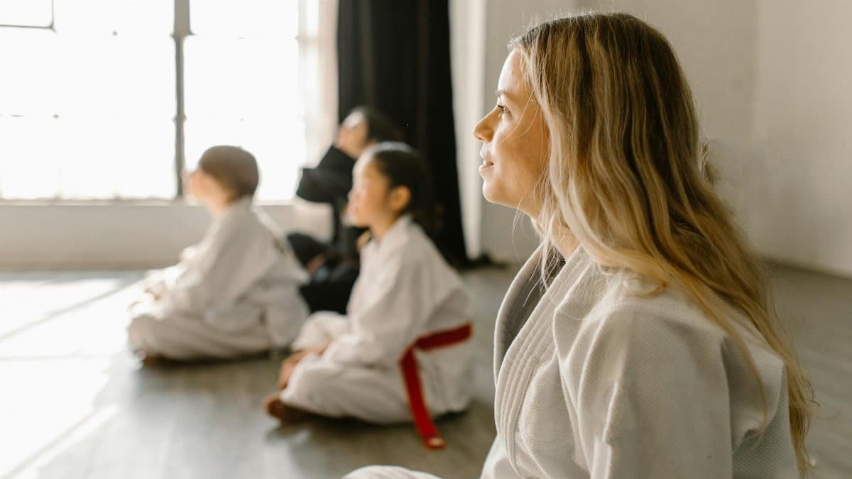 Children and adults attentively listening in a Taekwondo class session indoors.